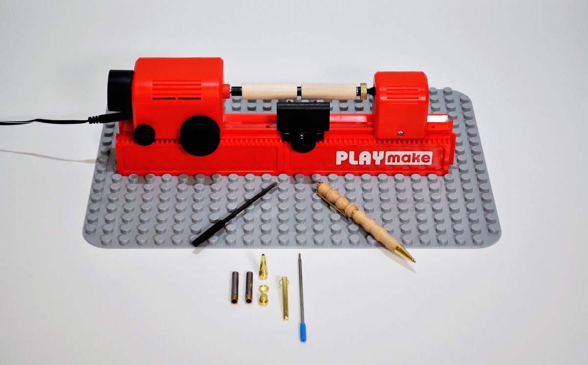 PLAYmake-Drechselbank mit zwei Holzrohlingen auf der Penmaker-Aufnahme, Stiftteilen und einem fertigen Holzstift.